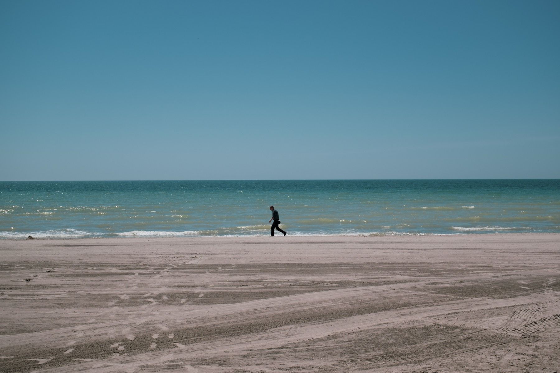 A lone figure walking beside the blue sea