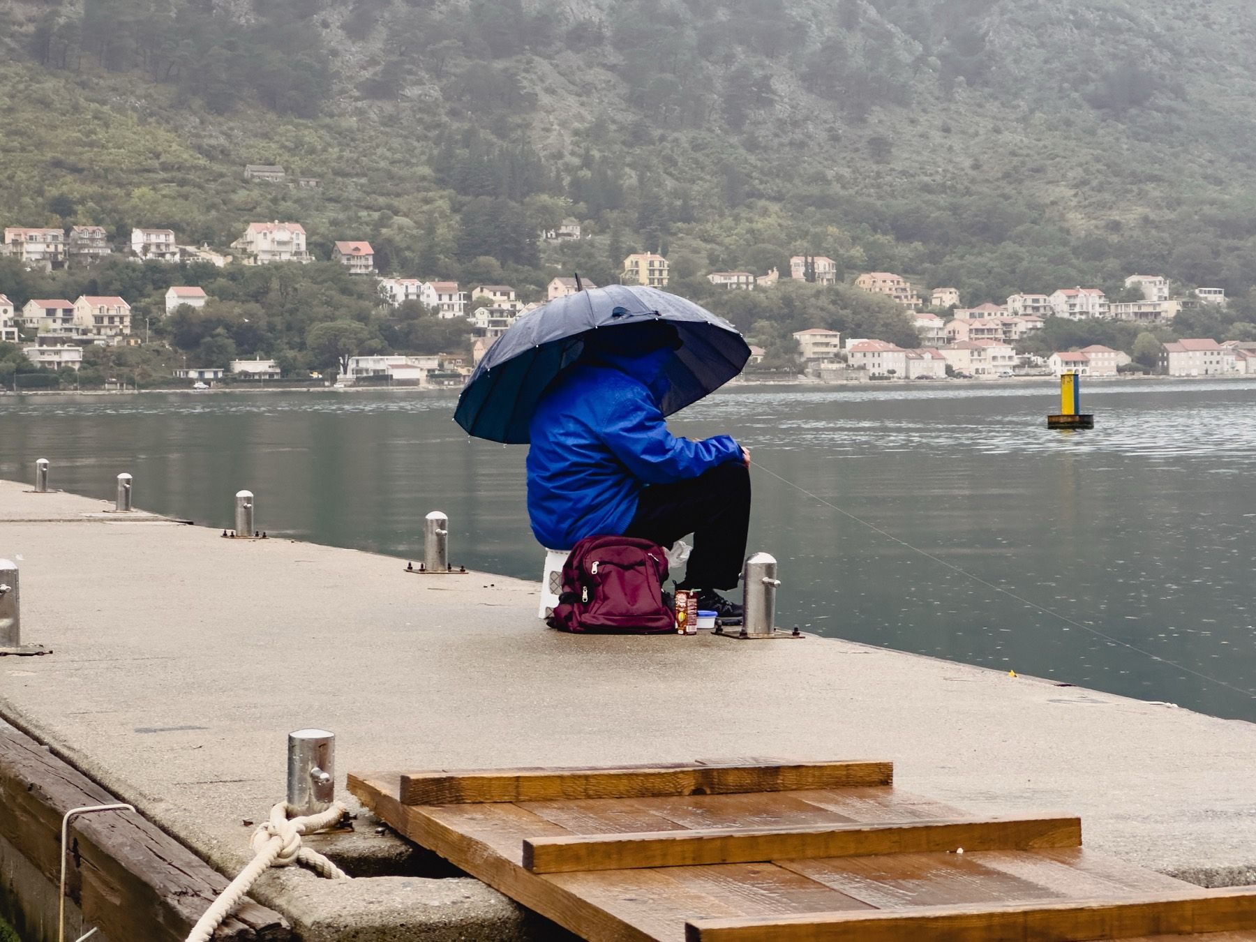 A fisherman sheltering beneath an umbrella